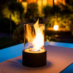 Oil lamp with open flame in clear glass cylinder on metal frame with decorative stones