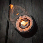 Oil lamp with open flame in clear glass cylinder on metal frame with decorative stones