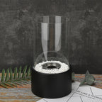 Oil lamp with open flame in clear glass cylinder on metal frame with decorative stones