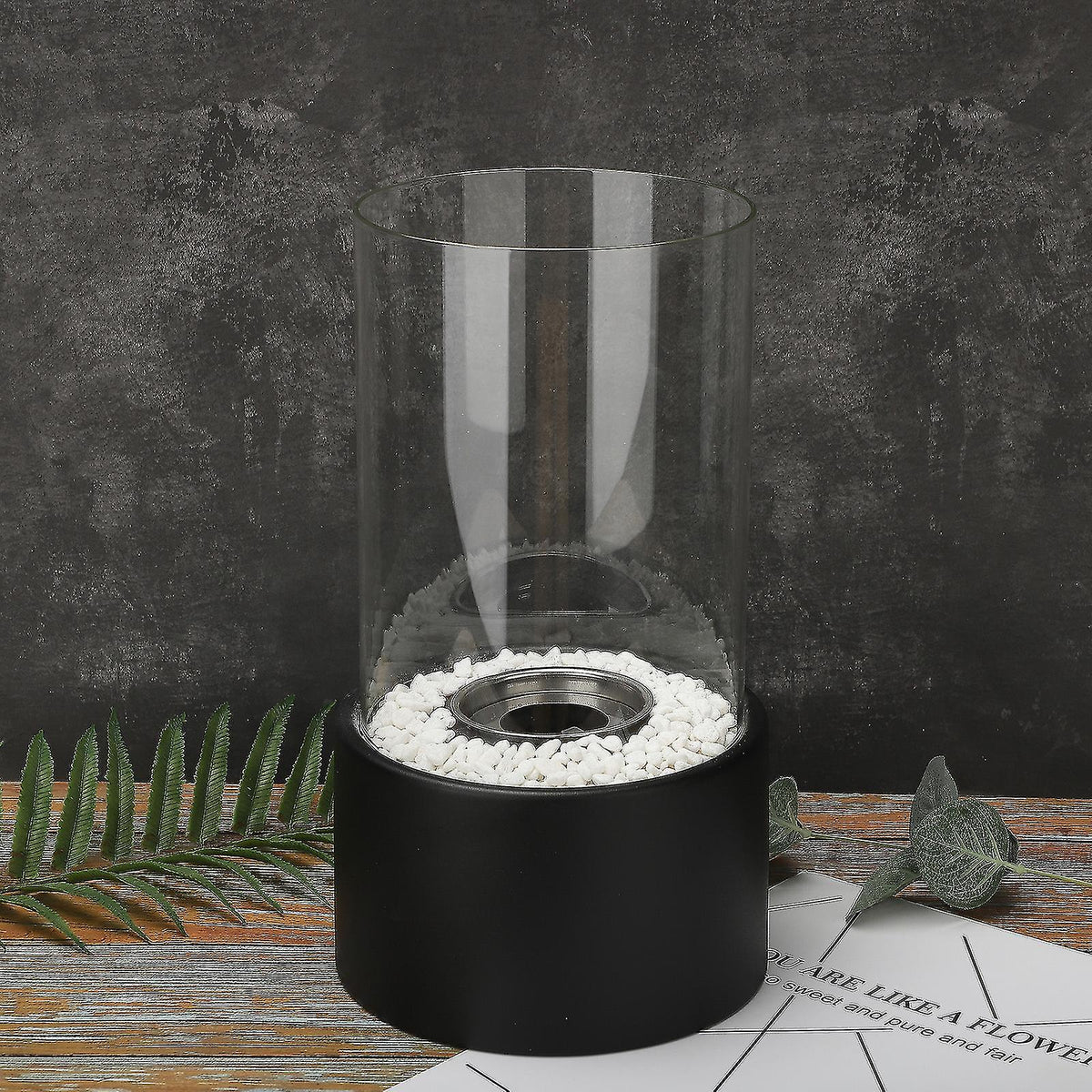 Oil lamp with open flame in clear glass cylinder on metal frame with decorative stones