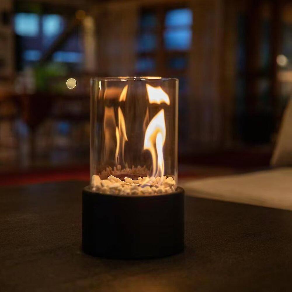 Oil lamp with open flame in clear glass cylinder on metal frame with decorative stones