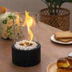 Oil lamp with open flame in clear glass cylinder on metal frame with decorative stones
