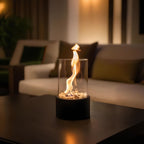 Oil lamp with open flame in clear glass cylinder on metal frame with decorative stones