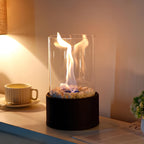 Oil lamp with open flame in clear glass cylinder on metal frame with decorative stones