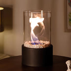 Oil lamp with open flame in clear glass cylinder on metal frame with decorative stones