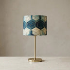 Table lamp with geometric patterned cylindrical shade and brass metal base, warm diffused light