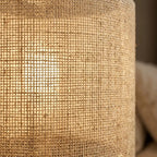 Table lamp with natural fabric cylinder shade and brass finish metal base, warm diffused light