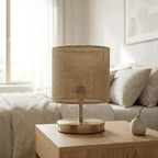 Table lamp with natural fabric cylinder shade and brass finish metal base, warm diffused light