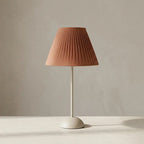 Table lamp with terracotta pleated fabric shade and slim pale matt metal base