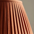 Table lamp with terracotta pleated fabric shade and slim pale matt metal base