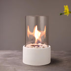 Oil lamp with open flame in clear glass cylinder on metal frame with decorative stones